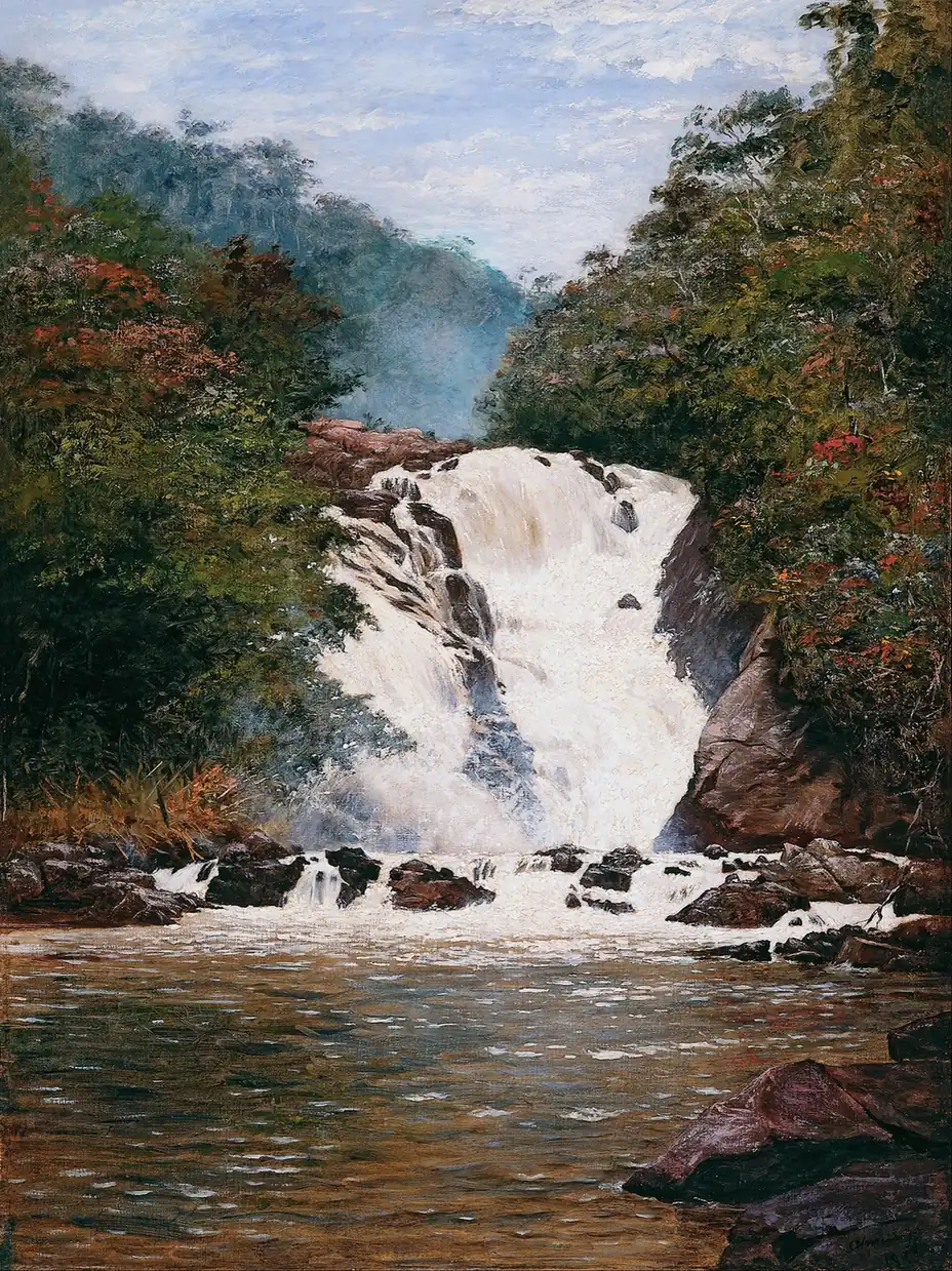 White, foaming waterfall tumbling between dark rocks and green forest with red flowers into a brown pool