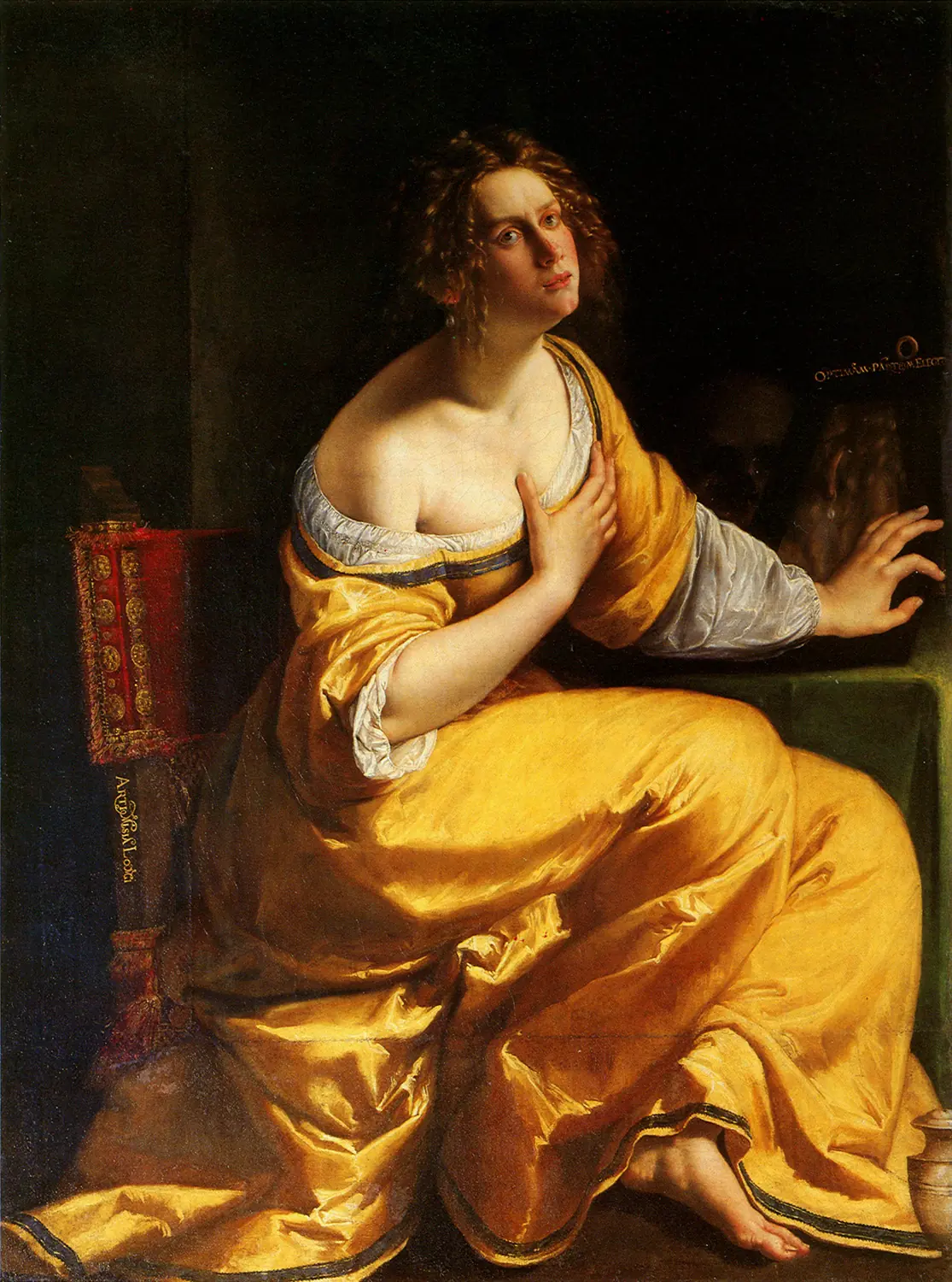 Mujer de vestido amarillo brillante, sentada, con una mano en el pecho y la otra apartando un espejo sobre una mesa