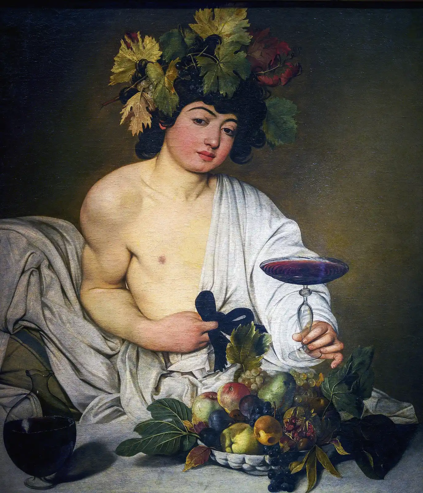 Joven coronado de hojas de vid que sostiene una copa de vino tinto, con un frutero lleno en primer plano