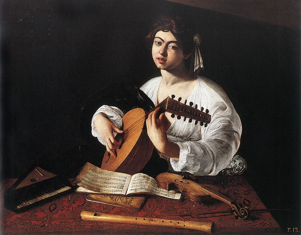 Joven de camisa blanca toca un laúd tras una mesa con libros de música, un violín, una flauta y un pequeño teclado