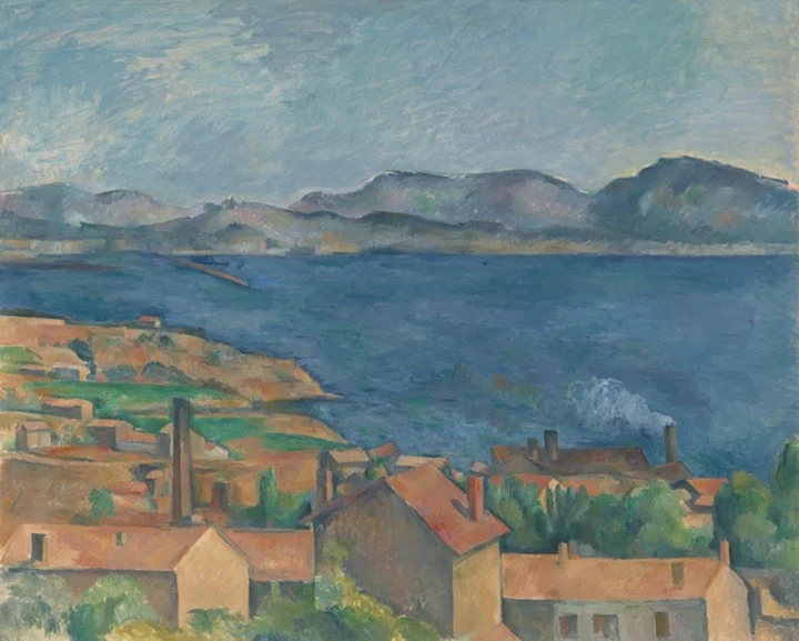 Orange rooftops and chimneys in the foreground, facing a bay of deep blue sea with mountains beyond