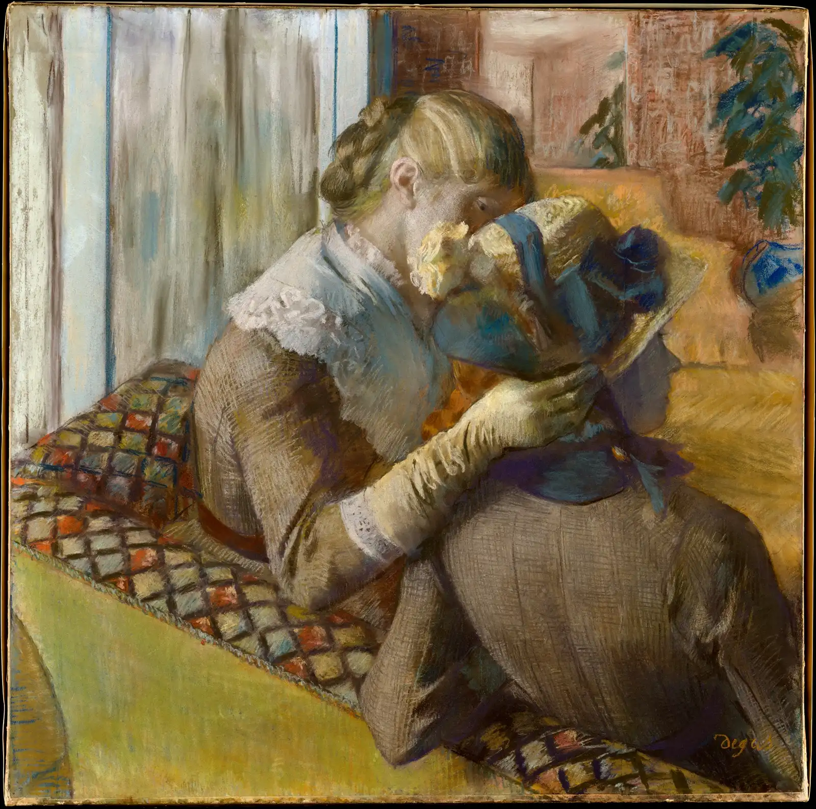 Woman in a brown dress and long gloves bringing her face close to a hat with blue ribbons, seated on a sofa