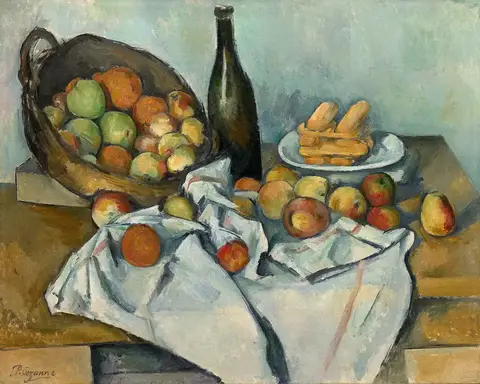 Canasta inclinada llena de manzanas, una botella oscura y un plato de bizcochos sobre una mesa con mantel blanco