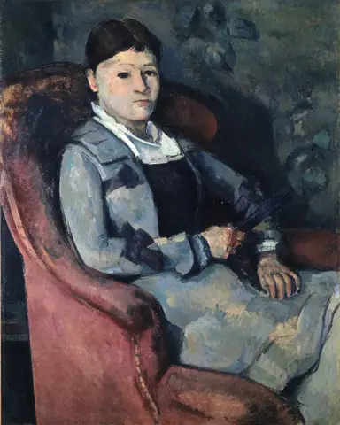 Mujer de chaqueta azul grisácea y cuello blanco sentada en un sillón rojo, con un abanico oscuro entre las manos