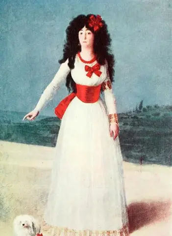 Woman standing in a white dress with red bows and sash, long black curls, pointing at the ground in open country