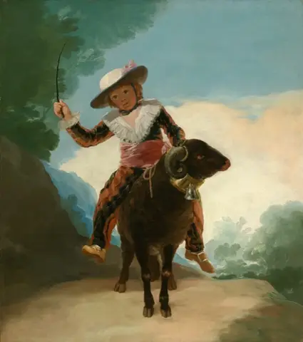 Boy in a wide-brimmed hat and diamond-patterned suit rides a dark ram on a dirt path, holding up a thin switch