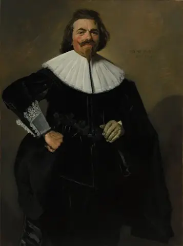 Hombre de pie vestido de negro, con gran cuello blanco, una mano en la cadera y un guante en la otra, sonriendo