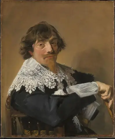 Hombre de cabello castaño y barba rojiza, sentado de lado, apoya el brazo en el respaldo de la silla y voltea a mirarnos