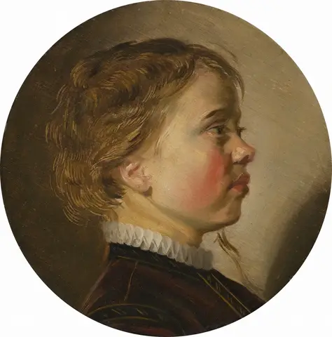 Niño de perfil, mirando hacia la derecha, con el pelo castaño claro y rizado y un cuello blanco, en formato redondo