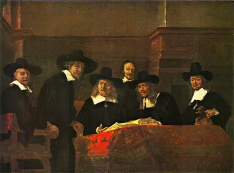 Seis hombres de negro, cinco con sombrero de ala ancha, reunidos tras una mesa con tapete rojo y un libro abierto