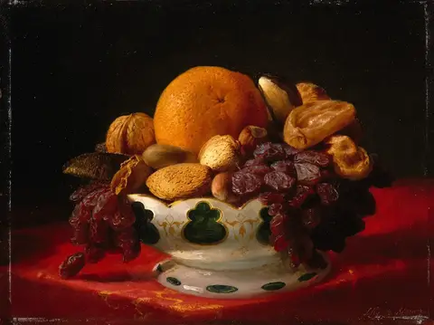 Orange, walnuts, almonds, dried figs and raisins in a white bowl with green decoration, on a red cloth