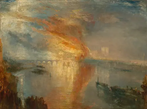 Gran incendio de llamas naranjas junto a un río con un puente de arcos, observado por una multitud en la orilla