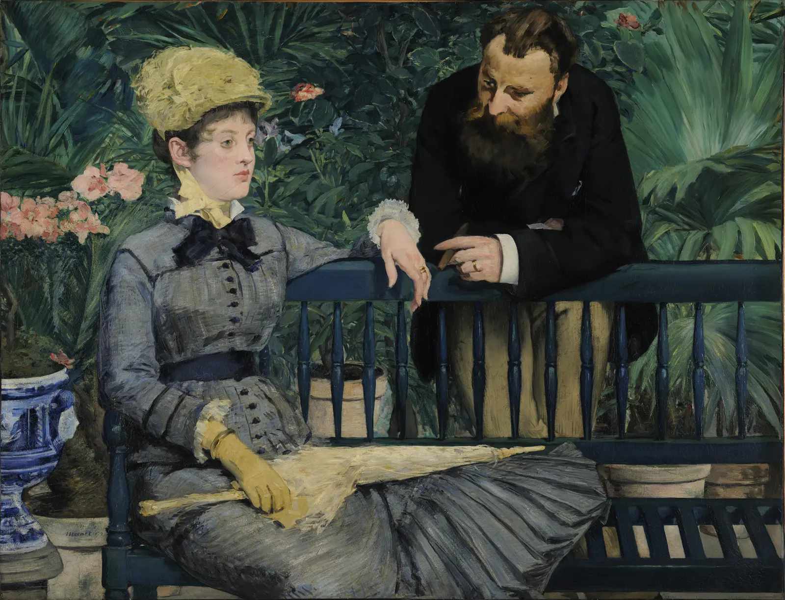 Woman in a gray dress seated on a dark bench while a bearded man leans on its back behind her, among plants