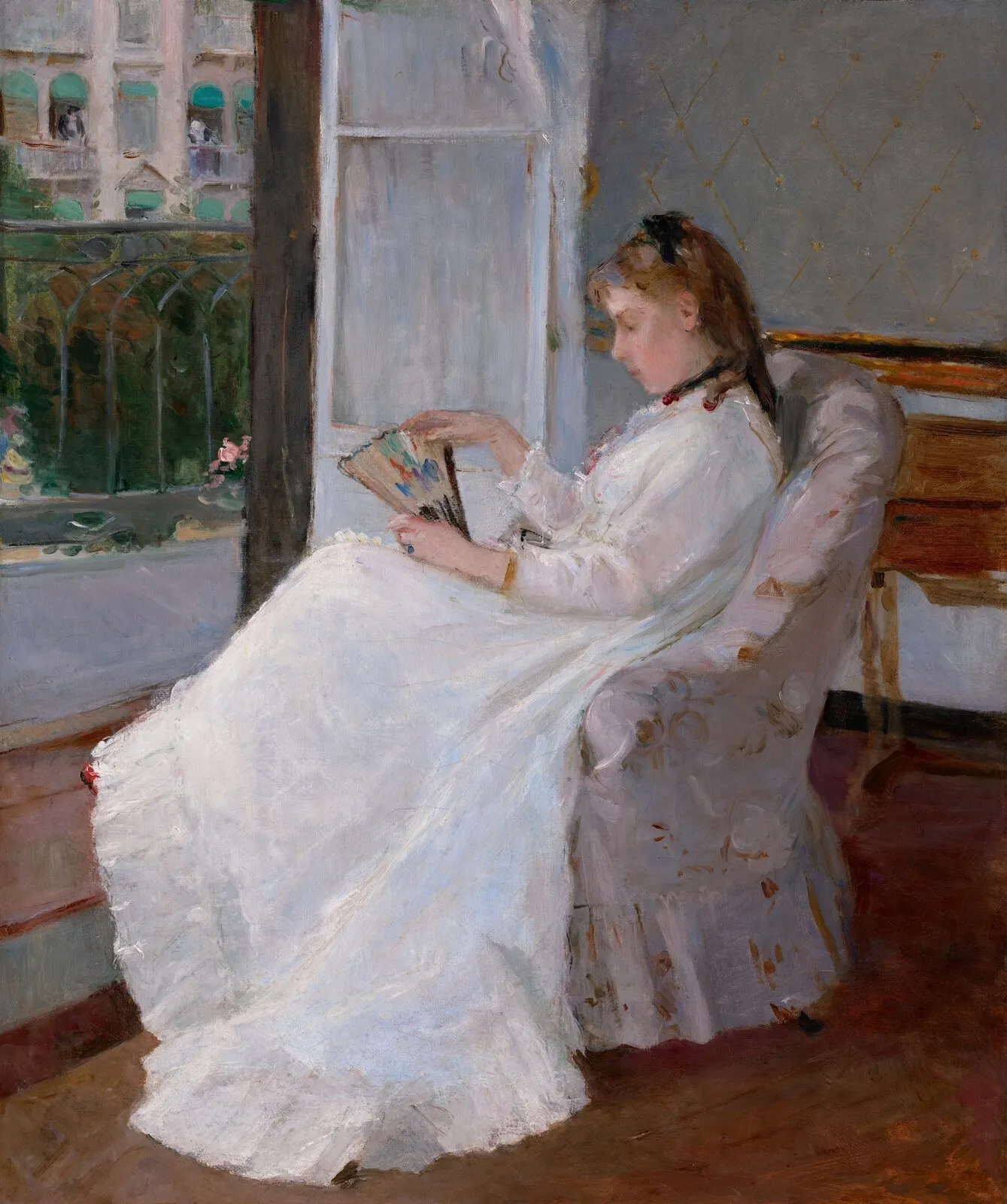 Young woman in a white dress seated in an armchair beside a door open onto a balcony, holding a fan