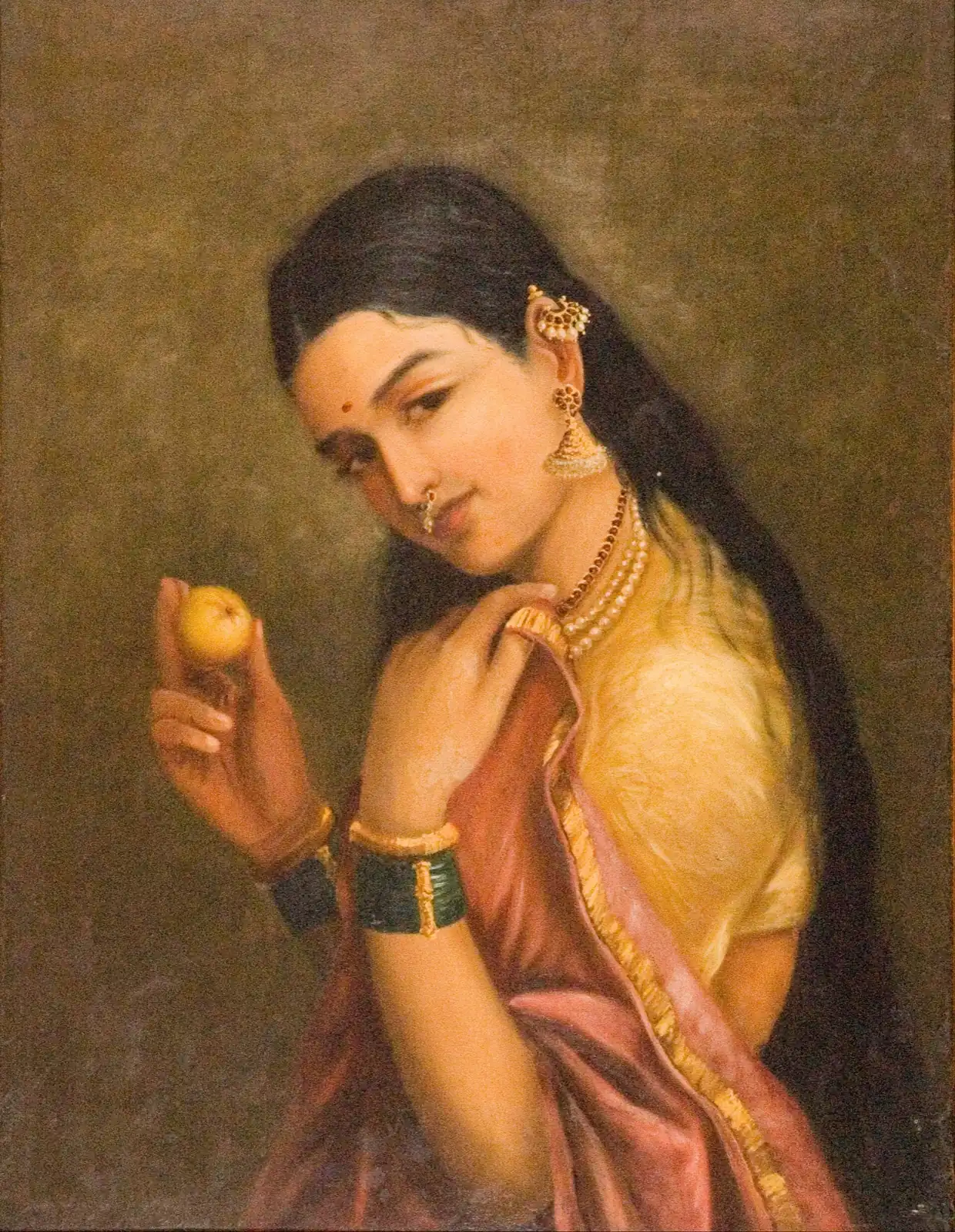 Mujer de cabello largo, blusa amarilla y sari rosa mira de reojo con la cabeza ladeada y una fruta amarilla en la mano
