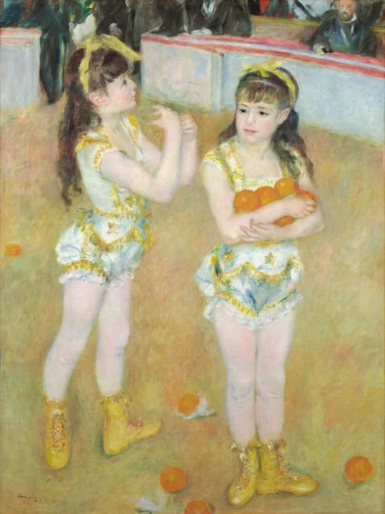 Dos niñas acróbatas con trajes blancos y dorados y botas amarillas en la pista de un circo, una con naranjas en brazos