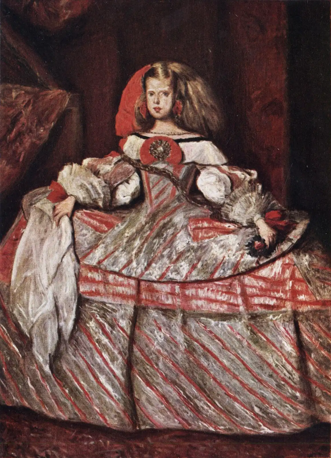 Niña de larga melena con adorno rojo y vestido muy ancho de rayas plateadas y rojas, con un pañuelo en la mano