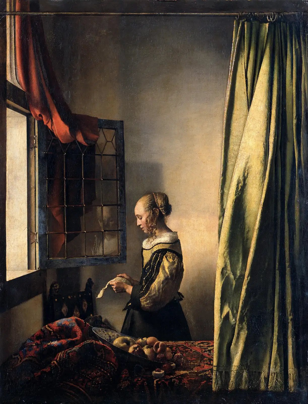 Young woman in profile reading a letter at an open window, a green curtain on the right and fruit on a rug